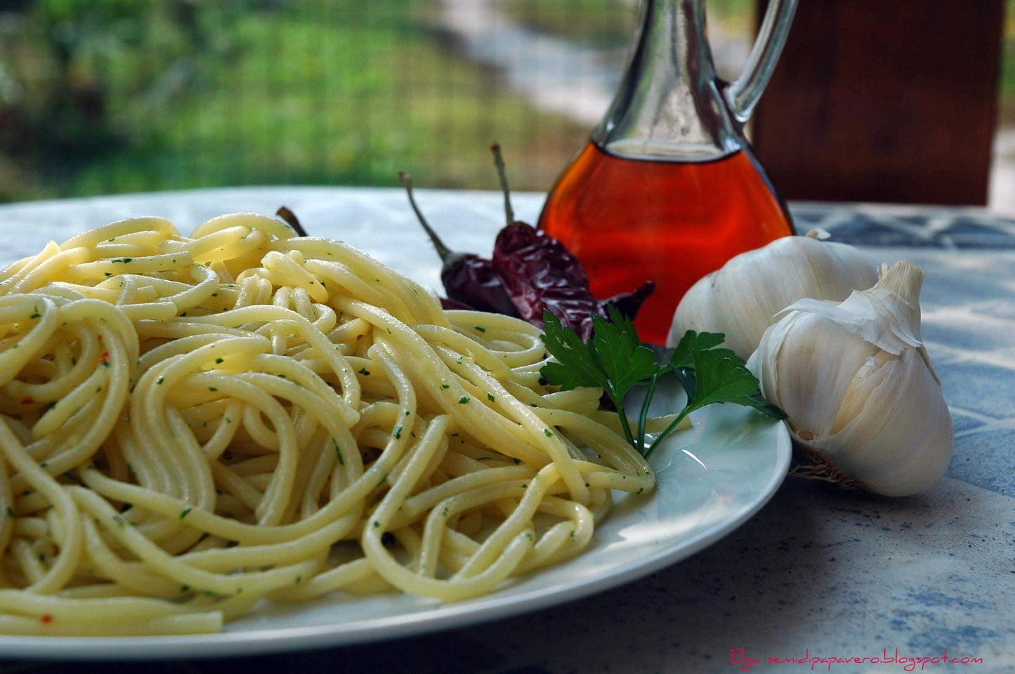 Colatura di Alici in a glass bottle next to spaghetti, garlic, and chili peppers on a plate.
