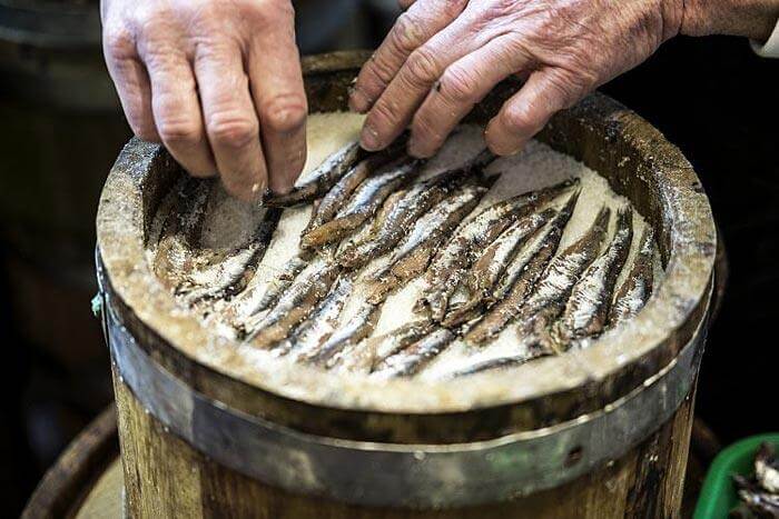 Colatura di Alici preparation process with salted anchovies in a wooden container.