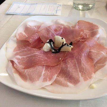 Culaccia di Modena artisanal sliced meat served on a white plate with cheese and garnishes.