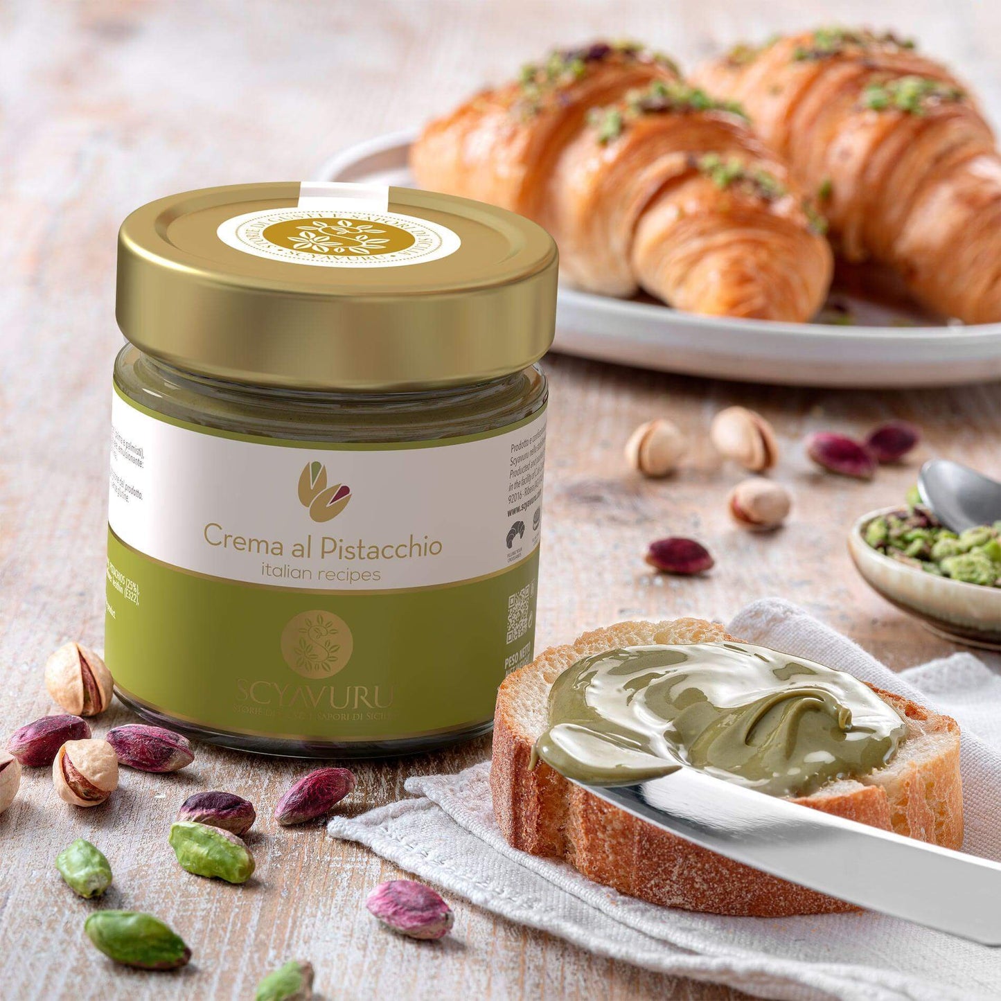 Crema spalmabile dolce di Pistacchio di Sicilia su una fetta di pane con croissant in sfondo.