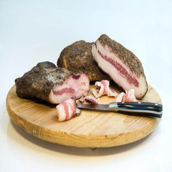Magulà - Guanciale Grecanico stagionato naturalmente e affumicato su un tagliere di legno con coltello.