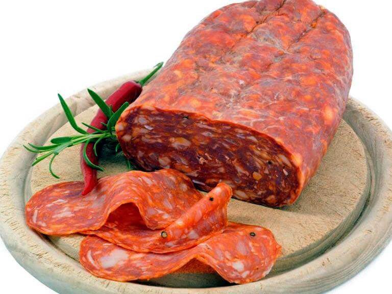 Spianata Piccante Calabrese sliced and whole, served with herbs and chilies on a wooden plate.