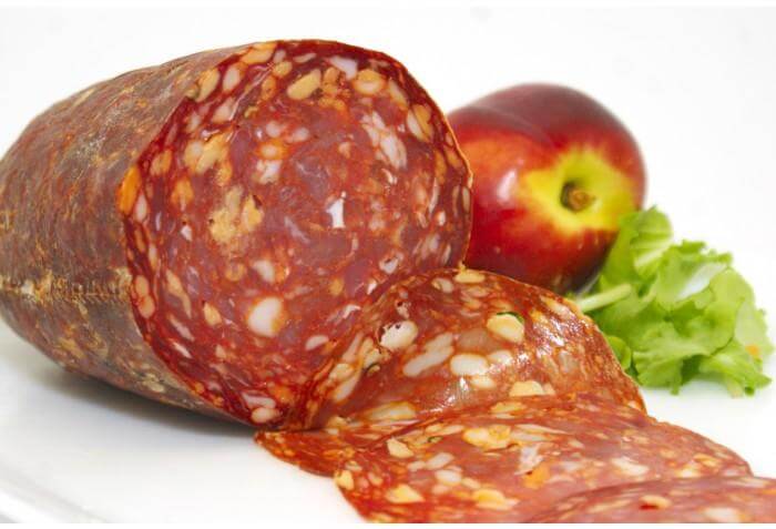 Sliced Ventricina Piccante Calabrese salami with apple and herbs on a white plate.