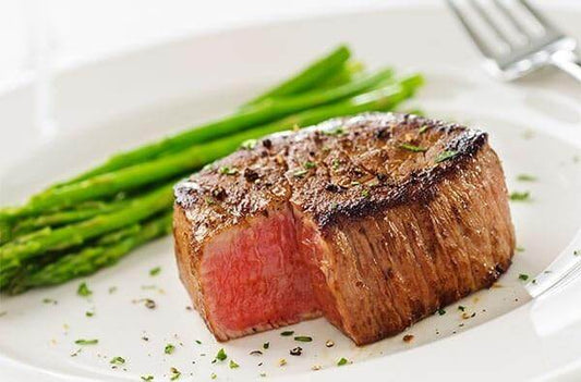 Perfectly cooked beef filet served with fresh asparagus garnished with herbs.