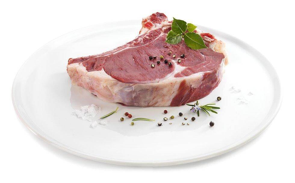 Raw beef rib steak with herbs and spices on a white plate, ready for grilling.