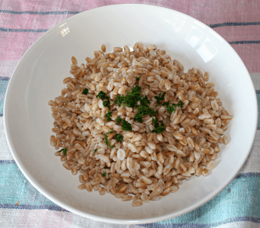 Bowl of cooked grains garnished with fresh parsley on a colorful tablecloth.