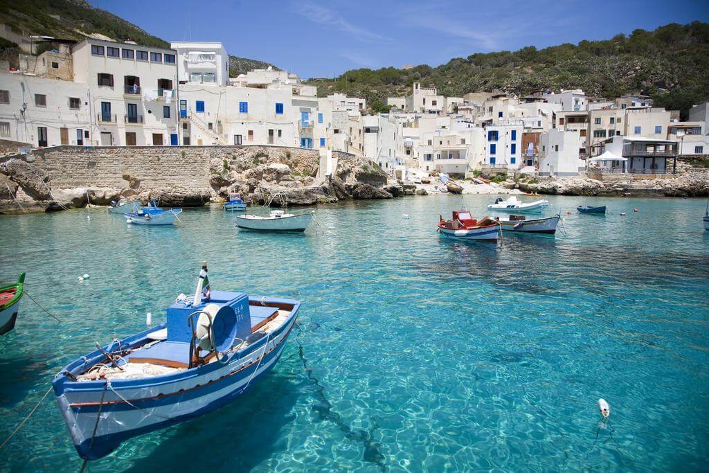 Porticciolo di Levanzo con barche colorate nel mare cristallino e case bianche sullo sfondo.