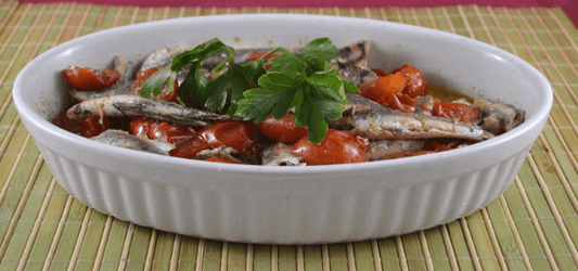Filetti di acciughe al pomodoro serviti in una ciotola con pomodorini e prezzemolo fresco.