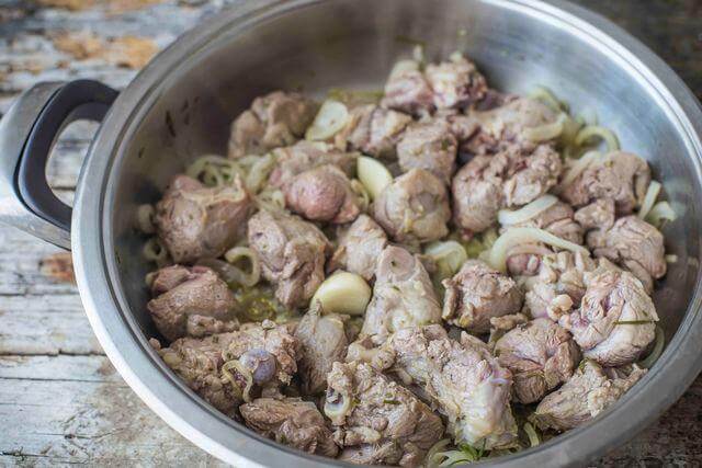 Tender pieces of capretto meat cooking with onions in a stainless steel pot.
