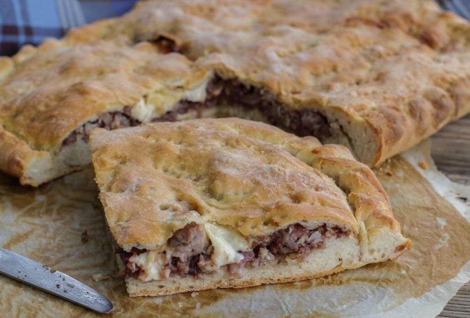 Slice of Sicilian focaccia filled with sausage and caciocavallo cheese on a wooden board.