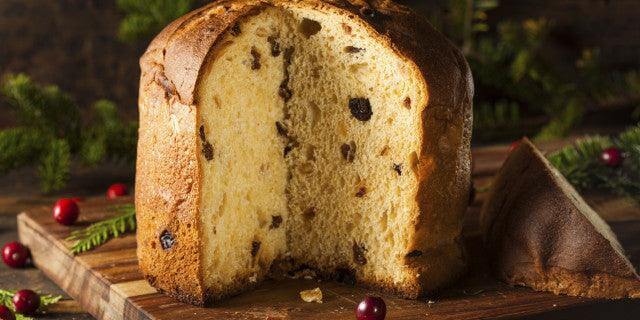 Sliced Panettone di Milano on a wooden board, showcasing its fluffy texture and colorful fruit pieces.