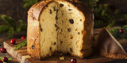 Sliced Panettone di Milano on a wooden board, showcasing its fluffy texture and colorful fruit pieces.