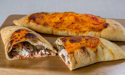 Delicious calzones with a golden crust, filled with cheese, meats, and vegetables, served on a wooden board.