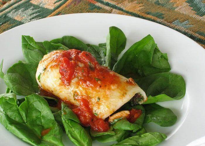Involtini di tonno su un letto di spinaci freschi, con salsa di pomodoro e formaggio, serviti in un piatto bianco.