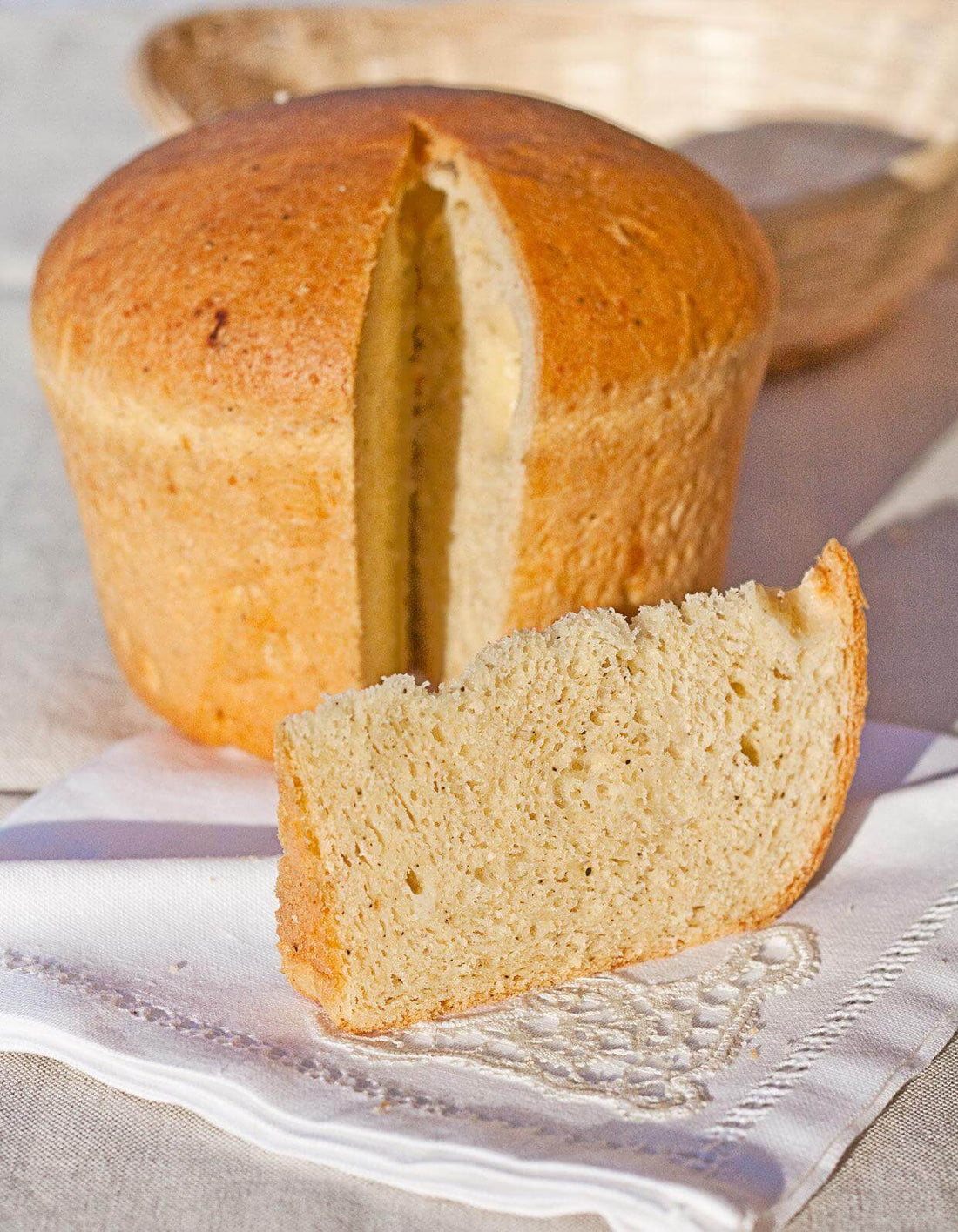 Freshly baked loaf of bread with a slice cut, displayed on a white linen cloth.