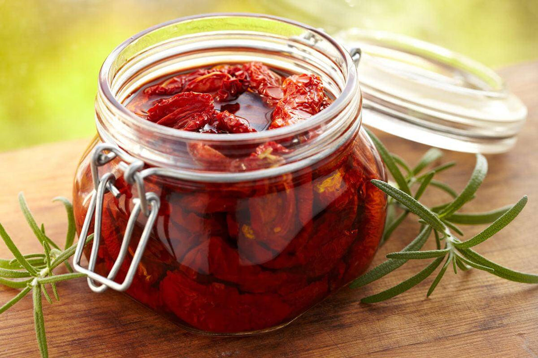 Jar of sun-dried tomatoes in olive oil with rosemary on a wooden surface.