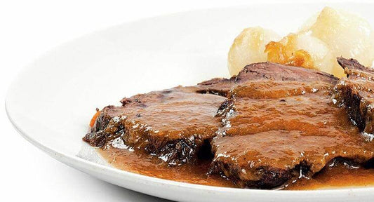 Delicious slices of beef in rich sauce served with a side of soft dumplings on a white plate.