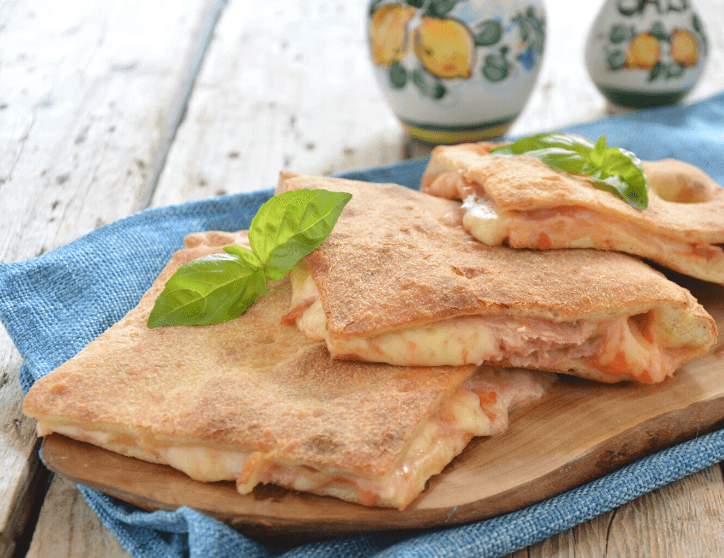 Pizza coperta on a wooden board, topped with fresh basil leaves and served on a blue cloth.
