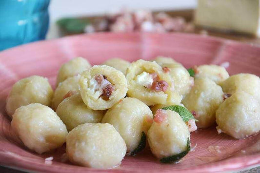 Gnocchetti a sorpresa with prosciutto and cheese served on a pink plate, garnished with sage.