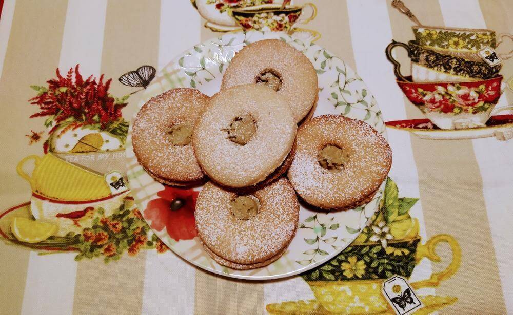 Delicious pistachio occhi di bue cookies dusted with powdered sugar on a decorative plate.