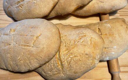 Freshly baked Calabrian bread loaves on a wooden surface, showcasing their crusty texture.