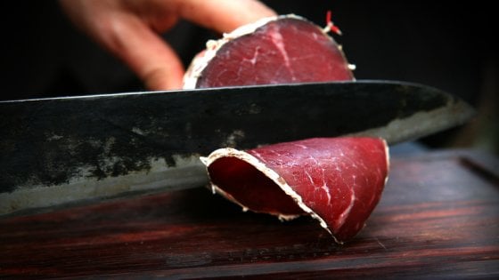 Salame di Capra being sliced with a knife, showcasing its rich red color and texture.