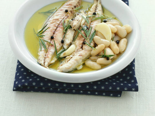 Filetti Sgombro al bergamotto su un letto di fagioli bianchi, con rosmarino e pepe in un piatto bianco.