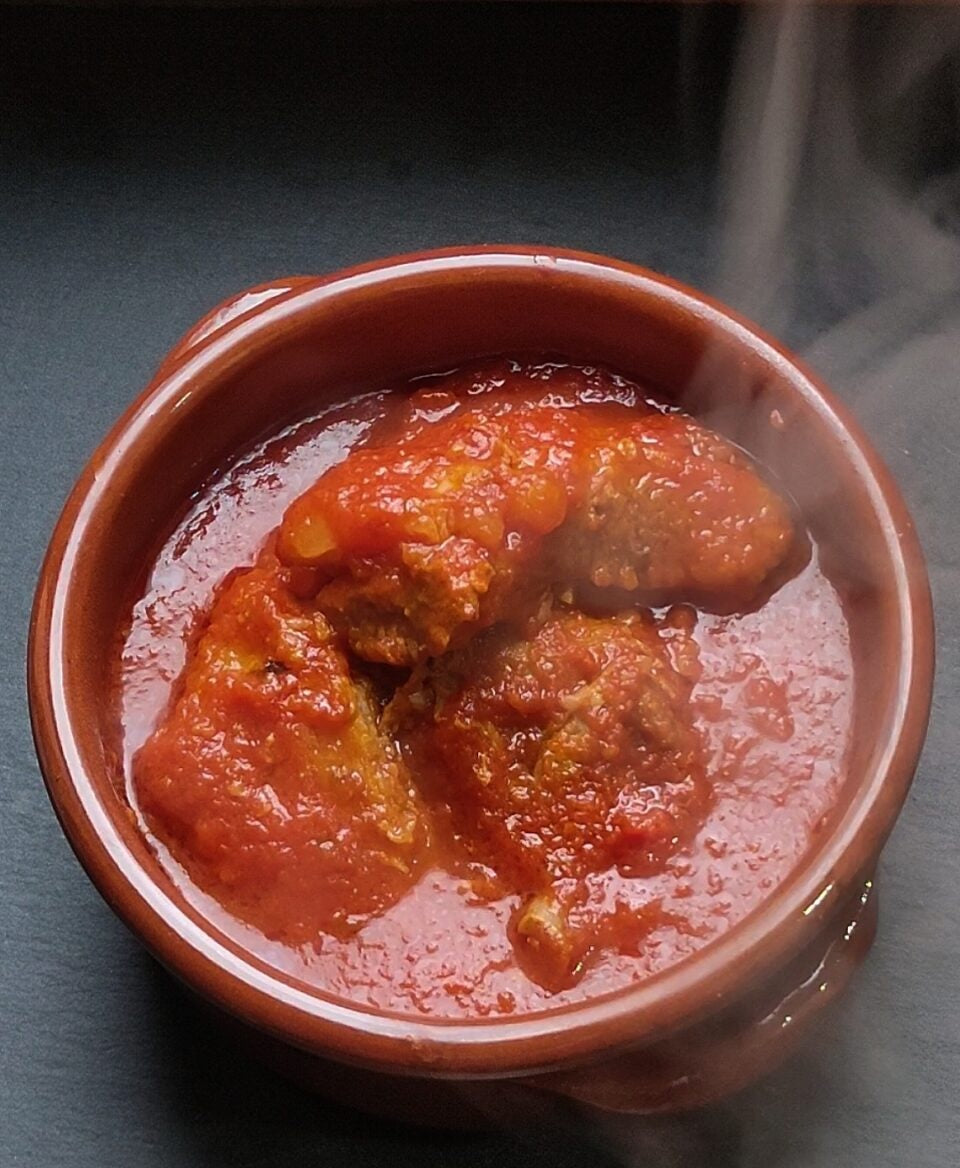 Ragù di maiale pronto alla calabrese in un contenitore di terracotta fumante, ricco di sugo di pomodoro.