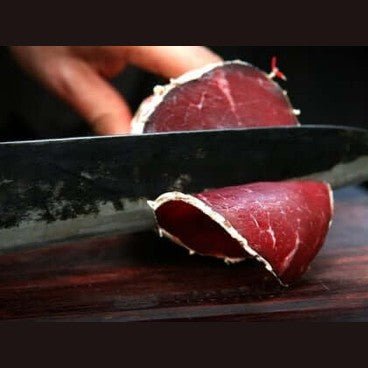 Salame di Capra being sliced with a knife, showcasing its rich red color and texture.