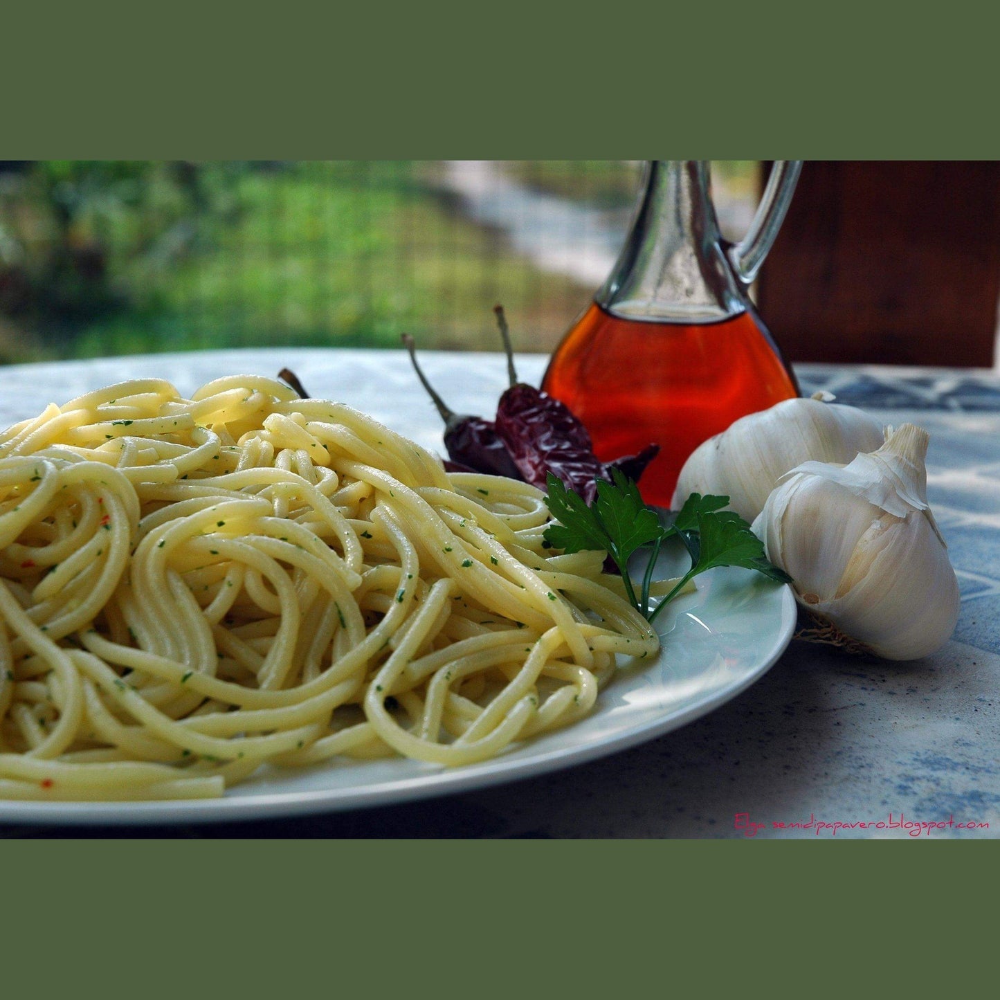 Colatura di Alici in a glass bottle next to spaghetti, garlic, and chili peppers on a plate.