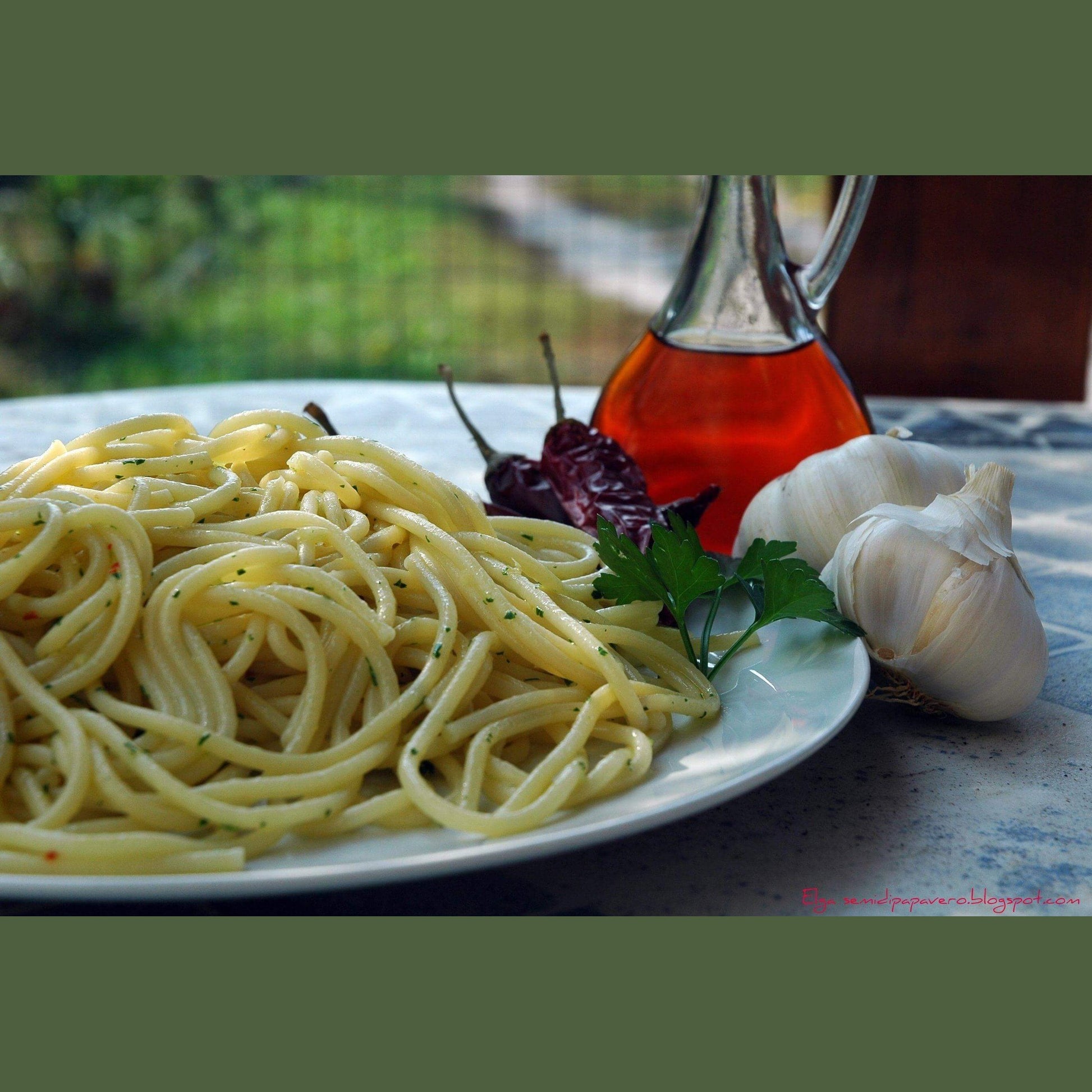 Colatura di Alici in a glass bottle next to spaghetti, garlic, and chili peppers on a plate.