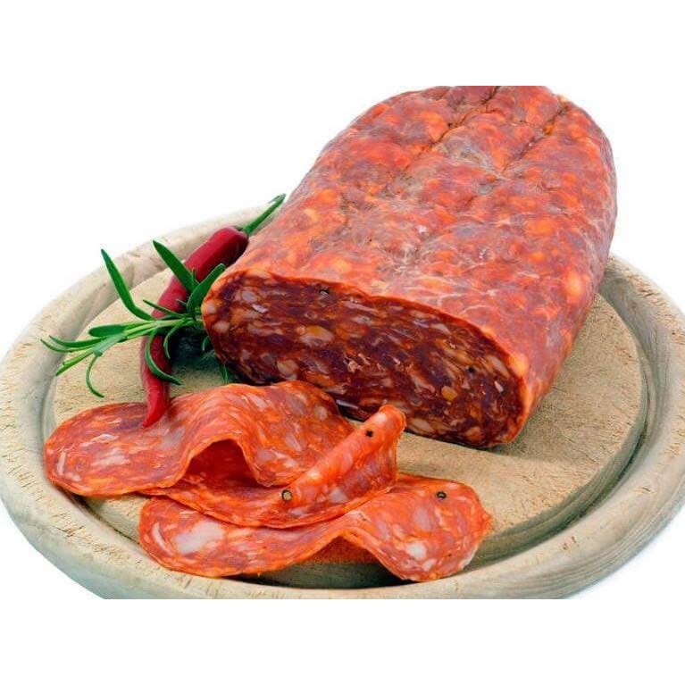 Spianata Piccante Calabrese sliced and whole, served with herbs and chilies on a wooden plate.
